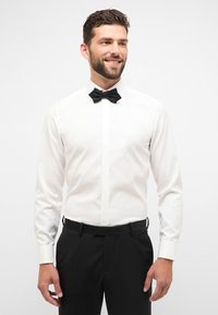 Witte overhemden met een geplooide voorkant en een zwarte vlinderdas, gecombineerd met zwarte broek. Gladde stof en klassieke pasvorm, zonder patronen.