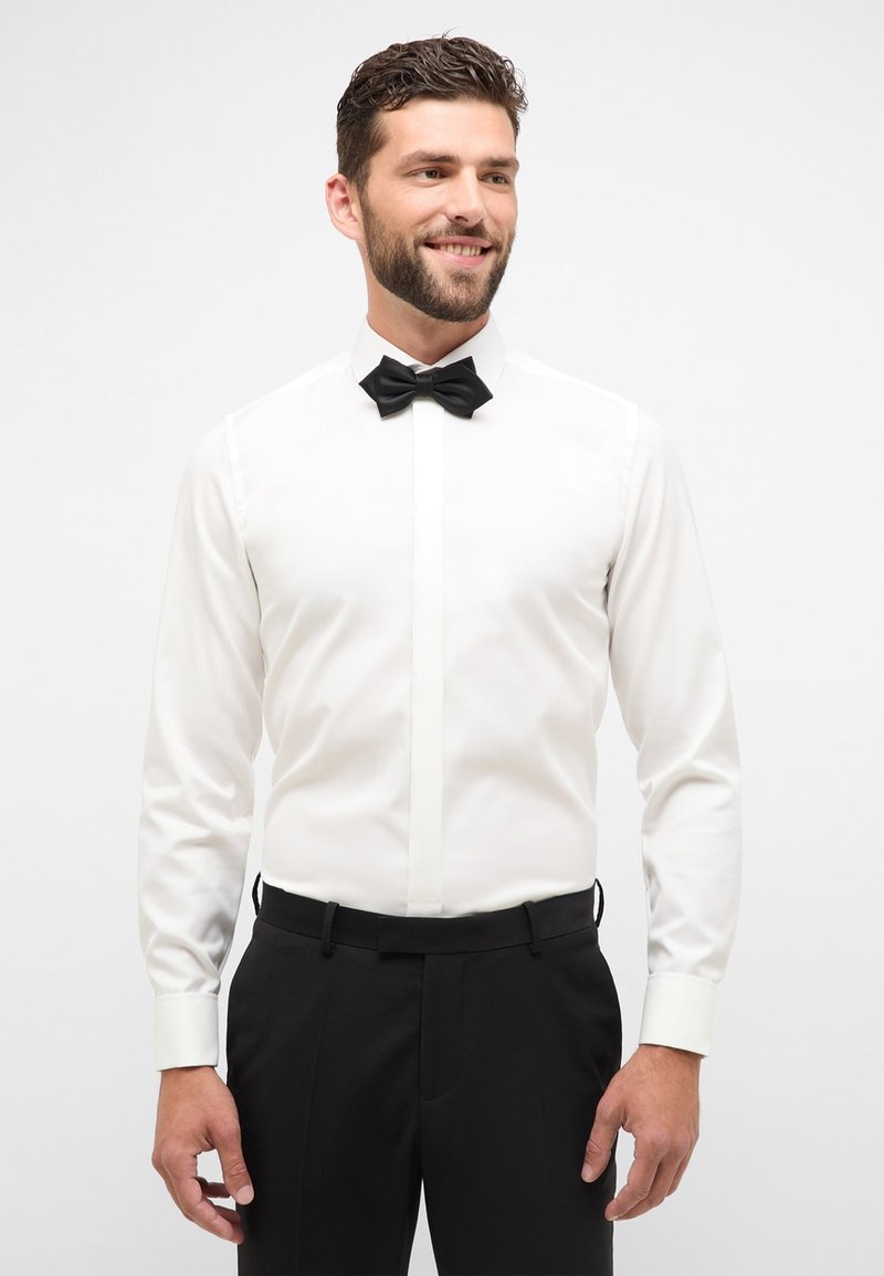 Witte overhemden met een geplooide voorkant en een zwarte vlinderdas, gecombineerd met zwarte broek. Gladde stof en klassieke pasvorm, zonder patronen.