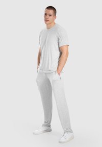 Hellgrau Baumwoll-T-Shirt mit kurzen Ärmeln, kombiniert mit passenden grauen Jogginghosen, die einen lockeren Schnitt und einen elastischen Bund haben. Weiße Sneaker.