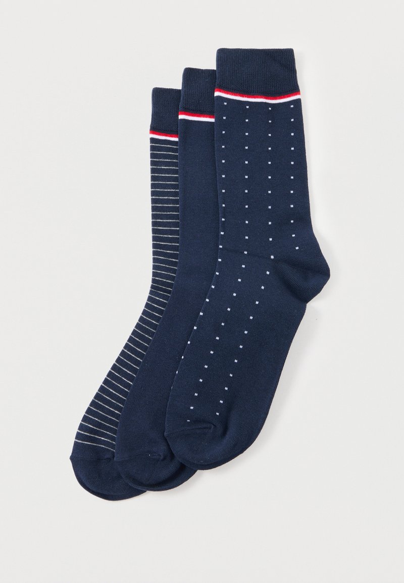 Trois paires de chaussettes bleu marine avec différents motifs : fines rayures blanches, couleur unie et petits pois blancs, chacune avec un bord rouge et blanc.