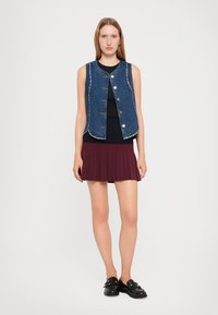 Denim veste ar spiedpogu aizdari un sudraba kniedēm, uzvilkts pār melnu krekli, saskaņots ar bordo svārku ar krokošanu, pabeigts ar melnām kurpēm.