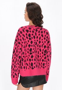 Maglione in maglia rosa con un motivo a leopardo nero, vestibilità comoda, spalle scese e orlo a coste. Indossato sopra una gonna in pelle nera.