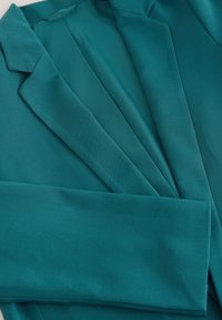 Teal blazer with a smooth texture, notched lapels, and an open front design. The fabric is lightweight, showcasing soft drapes and folds.