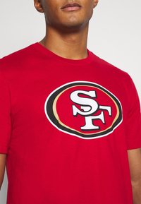 Rode katoenen t-shirt met een opvallend gedrukt ovaal logo met "SF" in het wit en zwart, omrand met goud. Korte mouwen, ronde hals ontwerp.