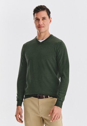 Zielony sweter w serek z długimi rękawami, wykonany z miękkiej tkaniny. Połączony z beżowymi spodniami i brązowym paskiem. Prosty, elegancki design.