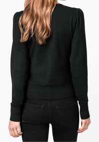 Svart stickad tröja med figurnära siluett och långa ärmar. Har puffiga axlar och ribbade ärmslut och fåll. Mjuk textur.