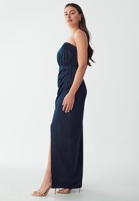 Námořnická strapless večerní šaty se skládacím živůtkem, bočním rozparkem a nařasením. Hladká látka s designem až na zem. Světlé boty na podpatku.