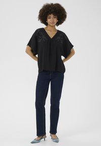 Fekete, plisszírozott felső virágmintás hímzéssel, V-kivágással, batwing ujjal, sötétkék egyenes szabású farmerrel és világoskék kiscicacipővel párosítva.