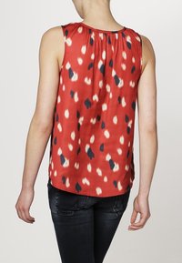 Top senza maniche rosso con motivi astratti neri e crema. Presenta un collo arricciato e una schiena drappeggiata, realizzato in un tessuto leggero.