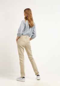 Vaaleanbeiget puuvillasekoitehousut, slim fit -malli takataskuilla, yhdistetty siniseen kuviolliseen puseroon ja valkoisiin tennekenkiin.