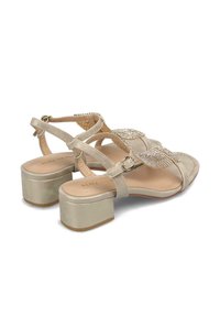 Sandalias en tono dorado con una correa decorativa que presenta acentos metálicos. Tacón medio grueso. Textura suave. Correa ajustable en el tobillo para un mejor ajuste.