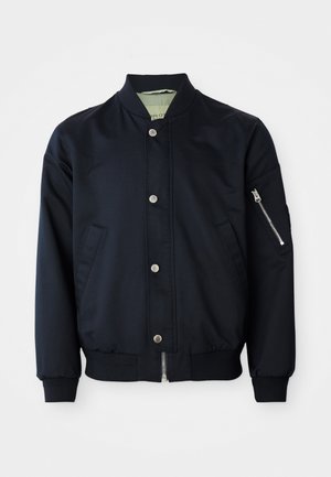 Chaqueta de bombardero navy con botones a presión, bolsillo con cremallera en la manga, cuello, puños y dobladillo de canalé, bolsillos frontales sobre fondo blanco.