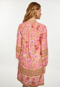 Rochie floral�ă roz cu mâneci lungi, spate plisat, modele decorative aurii și croi lejer.
