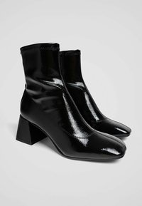 Černé lakované kotníkové boty se čtveratým podpatkem, elegantním designem a hladkým povrchem. Mají vysokou svršek a špičatou špičku.