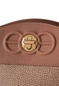 Sac à main en cuir marron avec une section inférieure texturée, une section supérieure lisse et un fermoir doré orné d'un logo et d'accents en design circulaire.