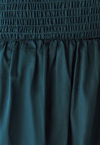 Tessuto smeraldo arricciato con texture plissettata, caratterizzato da una lucentezza morbida e da una vita elasticizzata per una vestibilità flessibile.
