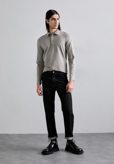 Světle šedé dlouhé polo s límcem a třemi knoflíky, v kombinaci s černými džínami a černými šněrovacími botami. Minimalistický design a přizpůsobený střih.