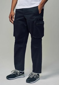 Pantalones cargo de color navy con varios bolsillos con cremallera, hechos de un tejido duradero, con un corte recto y detalles de costura visibles. Combinados con zapatillas negras.