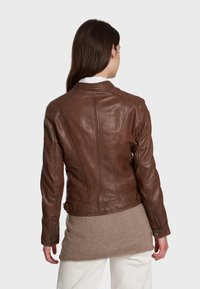 Brown leather jacket with a fitted design, featuring shoulder seams, a high collar, and zippered cuffs, worn over a light-colored top.