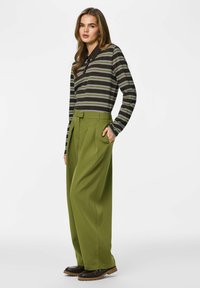 Tummanruskea pitkähihainen raidoitettu paita, jossa vihreitä, kerma- ja valkoisia raitoja; vyötäröltä korkeavyötäröiset oliivinvihreät housut; mustat kengät, joissa ruskeat pohjat.