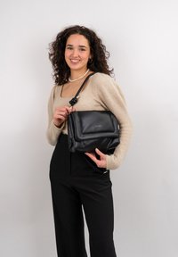 Černá kožená crossbody taška s klopou, detaily krouceného popruhu a jemným zlatým logem. Hladký povrch s pevným tvarem.
