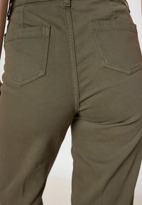 Un pantalon vert olive en tissu durable, à coupe décontractée, avec deux poches arrière dotées de surpiqûres solides. Le design présente une texture lisse.