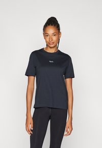 Schwarzes Baumwoll-T-Shirt mit kurzen Ärmeln, Rundhalsausschnitt und gesticktem Logo auf der Brust. Kombiniert mit schwarzen Leggings für einen stimmigen Look.