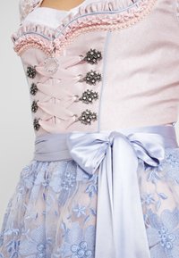 Corset rose pastel avec accents floraux argentés et devant à lacets. Ruban bleu satin à la taille, assorti à une jupe en tulle brodée bleue.