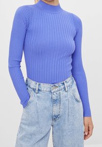 Jersey de cuello alto de manga larga con canalé en púrpura claro, combinado con vaqueros de cintura alta en azul claro que presentan un lavado desgastado y bolsillos frontales.