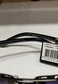 Occhiali da sole polarizzati neri con una montatura elegante, caratterizzati da testo inciso sulle astine e un'etichetta che mostra i dettagli del prodotto e il codice a barre.