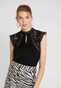 Zwarte top met kantmouwen, keyhole halslijn, gecombineerd met een zwart-witte zebraprint rok. Details omvatten ingewikkelde kantaccenten.