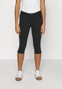 Jeans noirs cropped avec un design ajusté, présentant deux poches avant et une texture douce. Associés à des baskets blanches. Style minimaliste.