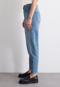 Jeans de tiro alto en azul claro con un corte recto, que cuentan con bolsillos frontales, bolsillos traseros y un desvanecimiento sutil. Combinados con unos zapatos negros sin cordones.