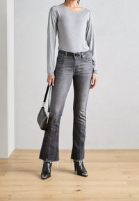 Graues Langarmoberteil kombiniert mit grauen, ausgestellt geschnittenen Jeans mit fransigen Säumen. Schwarze High-Heels und eine kleine schwarze Handtasche runden den Look ab.