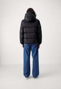 Sort pufferjakke med hætte, der har horisontale quiltede sektioner. Sammen med løse blå jeans og hvide sneakers.