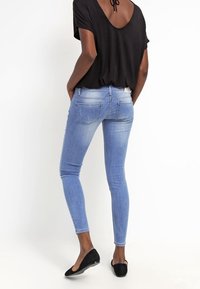 Jeans skinny de denim azul con un lavado desgastado, bolsillos traseros y una cinturilla. Combinados con una blusa negra de corte holgado y bailarinas negras.