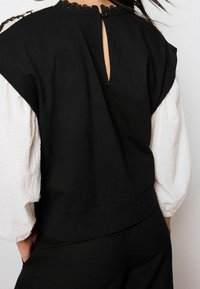 Top court noir avec de courtes manches bouffantes en tissu texturé blanc ; présente un col bordé de dentelle et une ouverture en keyhole à l'arrière.