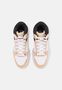 Paire de baskets montantes blanches et beige avec doublure intérieure noire et lacets blancs, vues de dessus sur un fond uni.