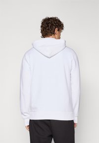 Hvit hettegenser med snor i hetten, ribbet mansjetter og kant, laget av mykt stoff. Baksiden viser et glatt, sømløst design.