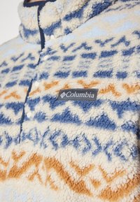 Πουλόβερ από fleece σε κρεμ, μπλε και πορτοκαλί χρώμα με γεωμετρικά σχέδια. Διαθέτει γιακά που στέκεται και λογότυπο Columbia στη θήκη του στήθους.