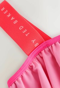 Roze zwemkleding met een geraffineerd ontwerp en een brede rode band met het label "by Ted Baker." De stof heeft een gladde textuur en een levendige kleur.