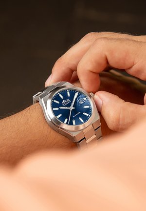 Reloj de acero inoxidable con esfera azul, marcadores de hora plateados y display de fecha. Presenta un bisel pulido y una pulsera de eslabones.