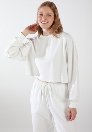 Weißer, kurzer Sweatshirt mit langen, gepufften Ärmeln und rundem Halsausschnitt, kombiniert mit passenden weißen Jogginghosen mit Kordelzug. Glatte Textur.