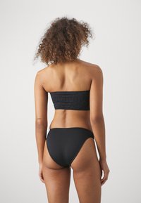 Juodas bikini komplektas, turintis tekstūruotą viršutinę dalį be petnešų su geometriniais raštais ir klasikinėmis aukštai talpomis, lygaus audinio apdaila.