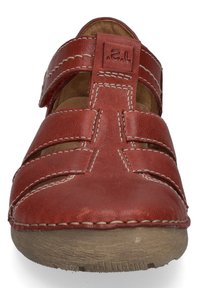 Red leather shoe with adjustable Velcro strap, open sides, and dark brown textured sole. Features white stitching and a rounded toe design.