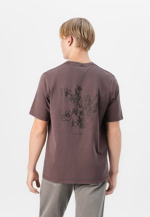 Brown cotton t-shirt with a relaxed fit, featuring a dark floral print on the back. Short sleeves and a rounded neckline.