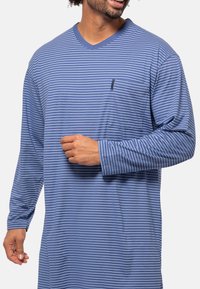 Camicia a maniche lunghe blu con righe orizzontali bianche, design a V, e taschino sul petto. Realizzata in tessuto morbido con una vestibilità comoda.