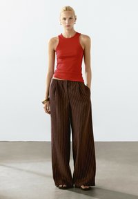 Rød ærmeløs bluse med en tætsiddende pasform, kombineret med løse brune pinstripede bukser med brede ben og frontfolder.