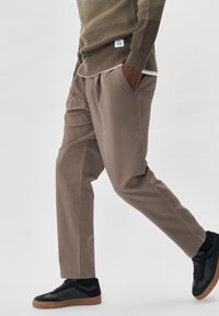 Beige kalhoty s uvolněným střihem, s bočními kapsami a elastickým pasem. V kombinaci s černými teniskami na texturované podrážce.