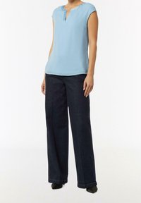 Top azzurro chiaro a maniche corte con scollo a V, abbinato a jeans svasati scuri. Texture liscia, design minimalista, vestibilità su misura.